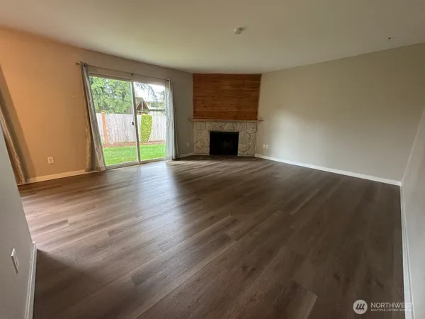an empty room with wooden floor fireplace and windows