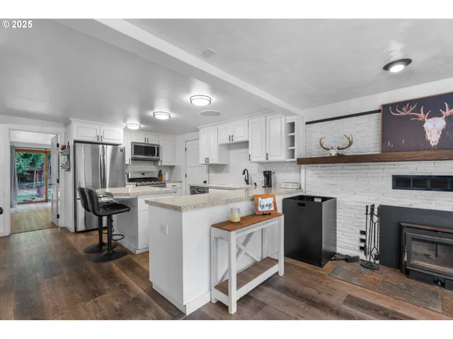 a kitchen with stainless steel appliances granite countertop a refrigerator a stove top oven a sink dishwasher and white cabinets with wooden floor
