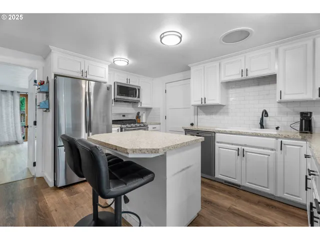 a kitchen with stainless steel appliances granite countertop a sink a stove a refrigerator and island with wooden floor