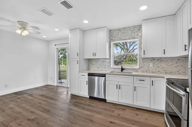 a kitchen with granite countertop a stove a sink and white cabinets with wooden floor