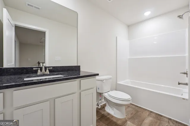 a bathroom with a granite countertop sink a toilet a mirror and shower