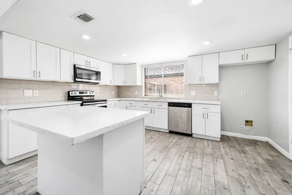 a kitchen with stainless steel appliances a sink dishwasher a stove top oven a refrigerator with white cabinets and wooden floor