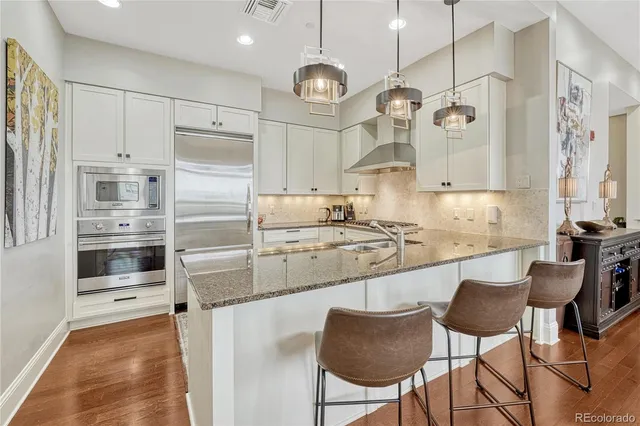 a kitchen with stainless steel appliances granite countertop a sink refrigerator a stove a dining table and chairs with wooden floor