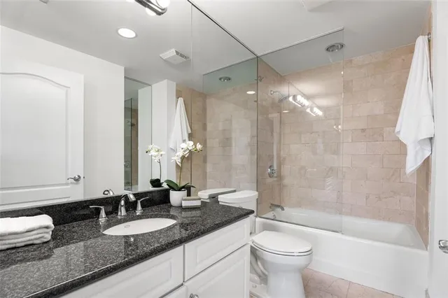 a bathroom with a granite countertop sink a toilet a mirror and shower