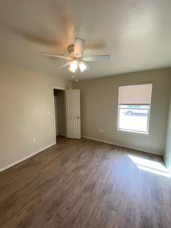 an empty room with wooden floor chandelier fan and windows
