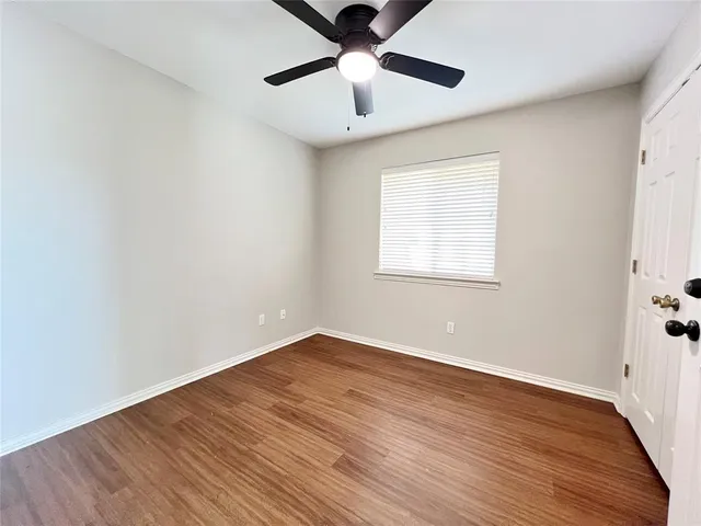 an empty room with wooden floor chandelier fan and windows
