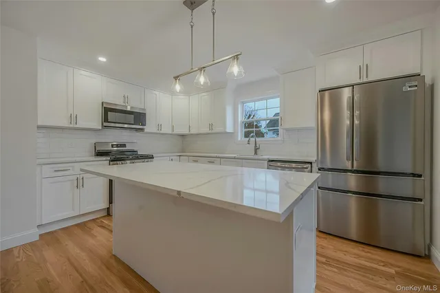 a kitchen with kitchen island granite countertop a refrigerator a sink dishwasher a stove and white cabinets with wooden floor