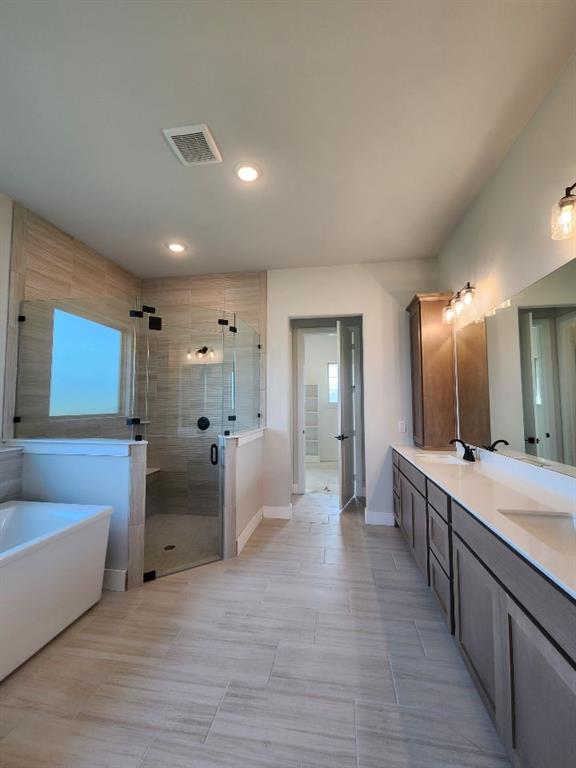 2305 Gypsum Street Krum, TX 76249 - Photo 16 of 22 Spacious bathroom featuring a freestanding tub, glass-enclosed shower with bench, dual vanity with undermount sinks, and large format tile flooring