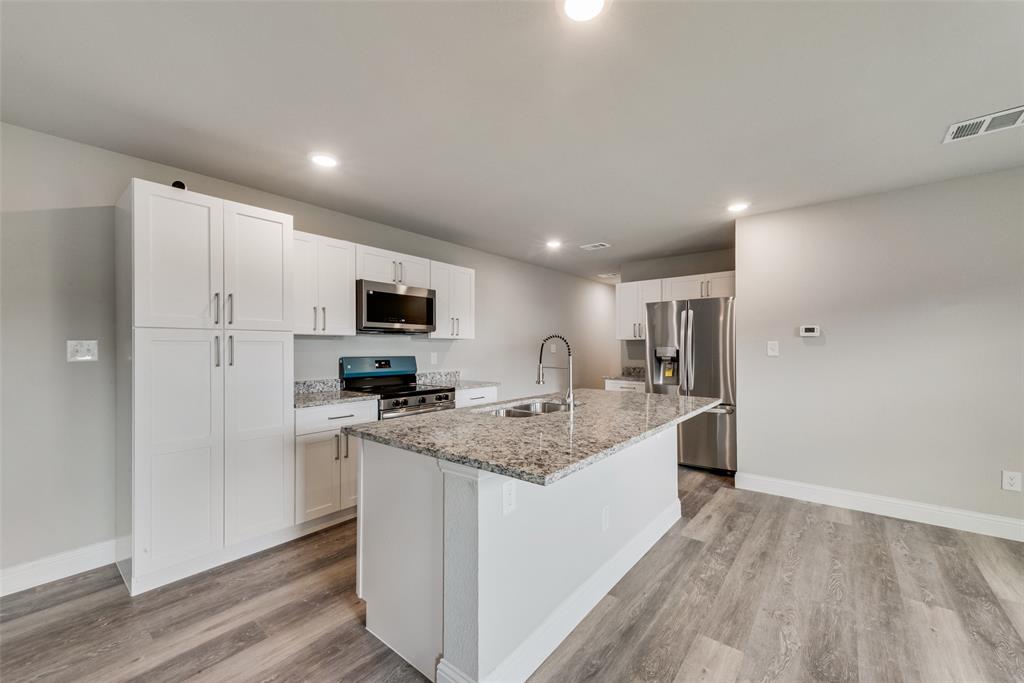 3153 Stag Road Dallas, TX 75241 - Photo 7 of 15 a large kitchen with a stove a sink dishwasher a refrigerator and white cabinets with wooden floor