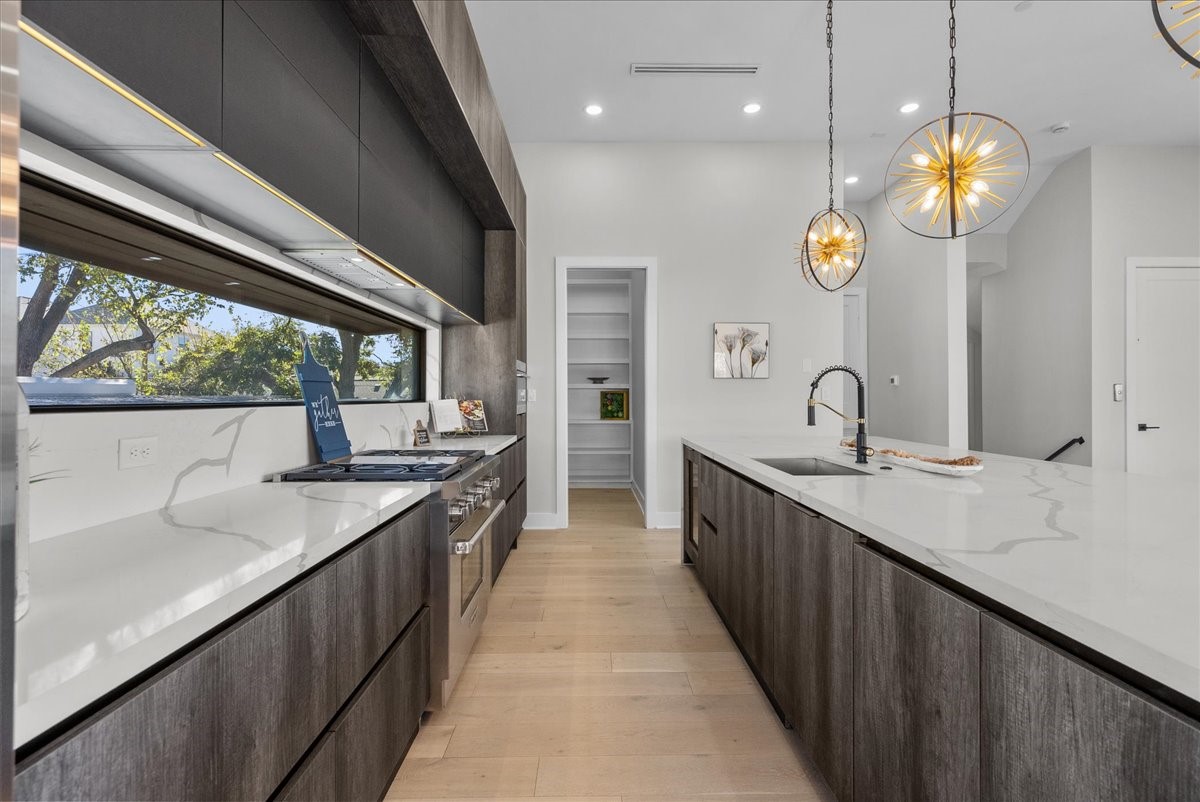 516 Reinerman Street Houston, TX 77007 - Photo 14 of 42 This modern kitchen features sleek dark cabinetry, light wood floors, and an expansive white countertop with a built-in sink. Large windows provide ample natural light, while contemporary pendant lights add elegance. A spacious pantry is accessible through a nearby door.