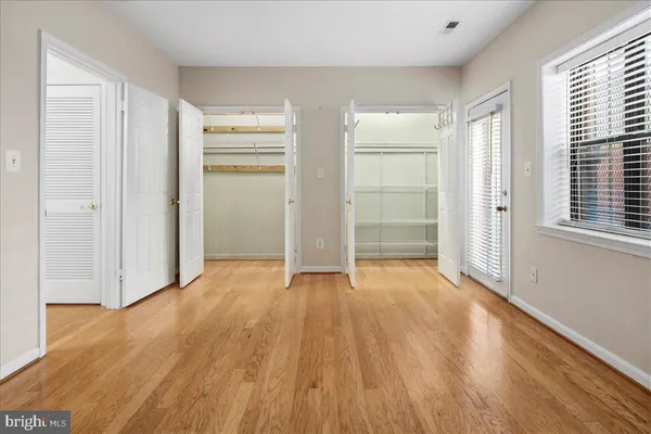 an empty room with wooden floor closet and windows