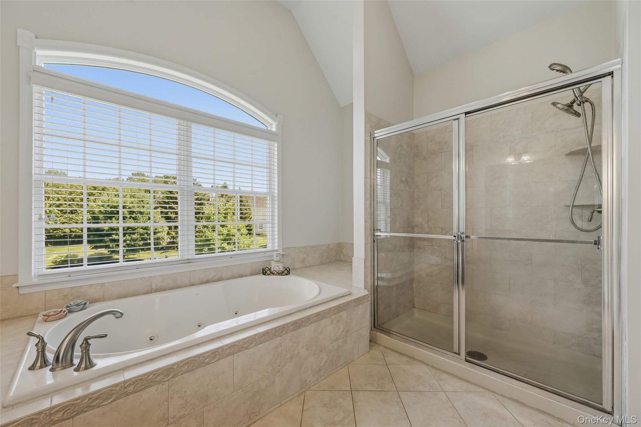 51 Meriwether Trail Congers, NY 10920 - Photo 26 of 50 Soaking tub with jetted features, a large arched window, a tiled shower enclosure with sliding glass doors, a dual shower head system, and tiled flooring