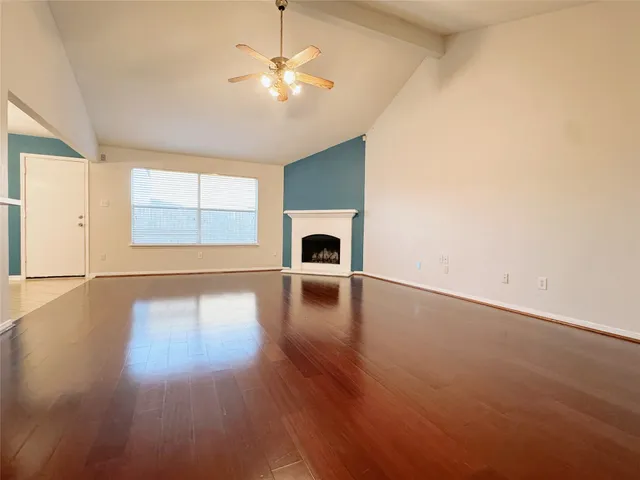 an empty room with wooden floor chandelier fan and windows