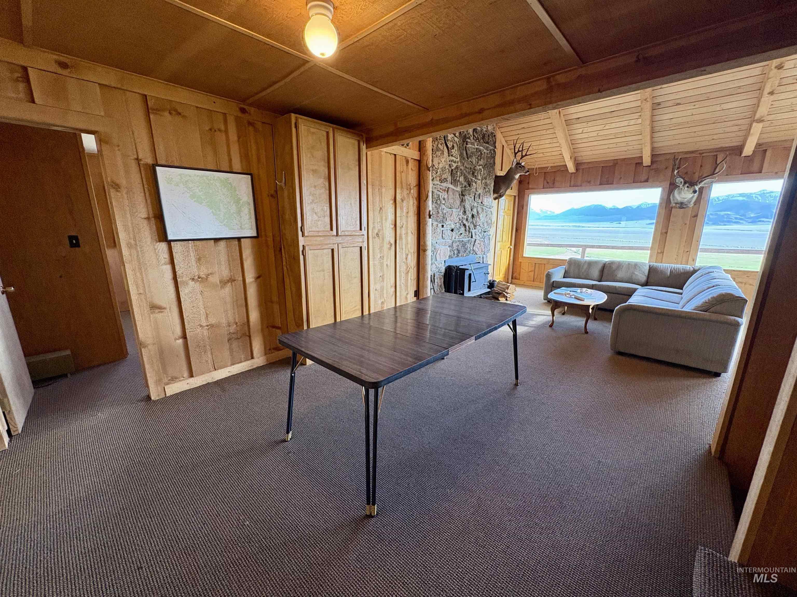 2040 Pahsimeroi River Road May, ID 83253 - Photo 14 of 29 Spacious room featuring wood paneling, a stone fireplace, and panoramic windows showcasing a mountain and water landscape