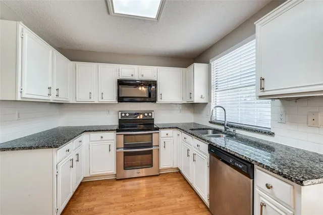 a white kitchen with granite top and stainless steel appliances