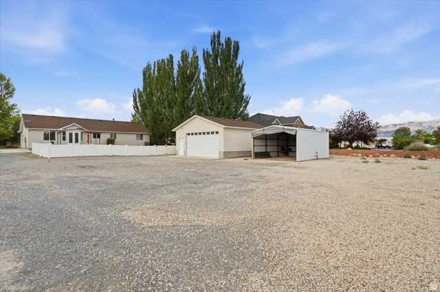 791 East Saddle Road Grantsville, UT 84029 - Photo 42 of 46 Expansive gravel lot featuring a detached garage with an overhead door, an open-sided metal carport, and a white privacy fence bordering the main residence