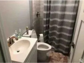 684 East 400 North Logan, UT 84321 - Photo 10 of 27 Bathroom featuring a vanity with an integrated sink, a toilet, a shower area with tiled walls, and a shower curtain