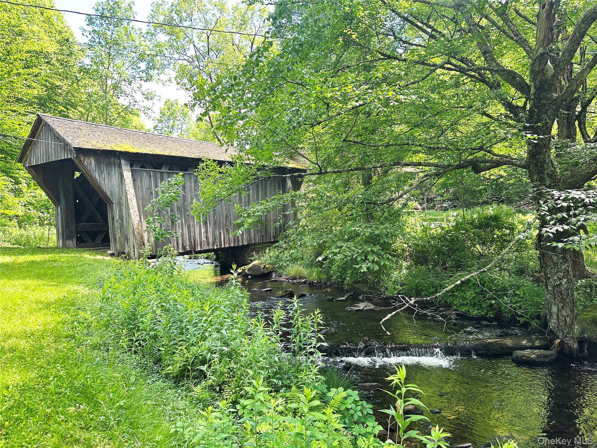 818 Methol Road Roscoe, NY 12776 - Photo 9 of 39 Side view of the historic covered bridge spanning Trout Brook, surrounded by lush greenery and scenic Catskills landscape.