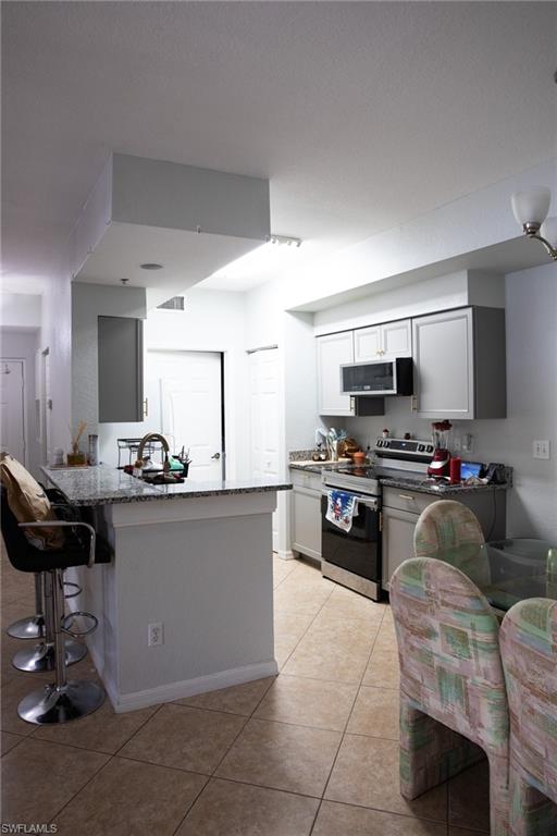 4650 St Croix Lane, Unit 726 Naples, FL 34109 - Photo 15 of 15 Kitchen with dark stone counters, stainless steel appliances, a breakfast bar area, and light tile patterned flooring