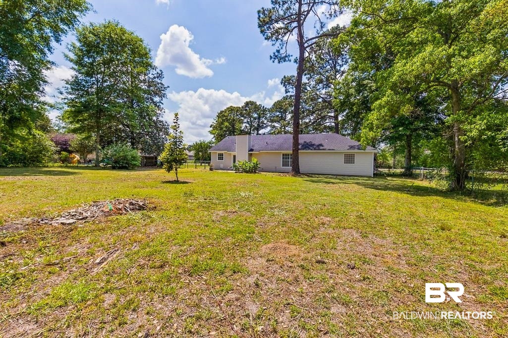 1301 Repoll Road Mobile, AL 36695 - Photo 19 of 21 Spacious backyard featuring a large grassy area, mature trees, and a distant single-story structure with light-colored siding