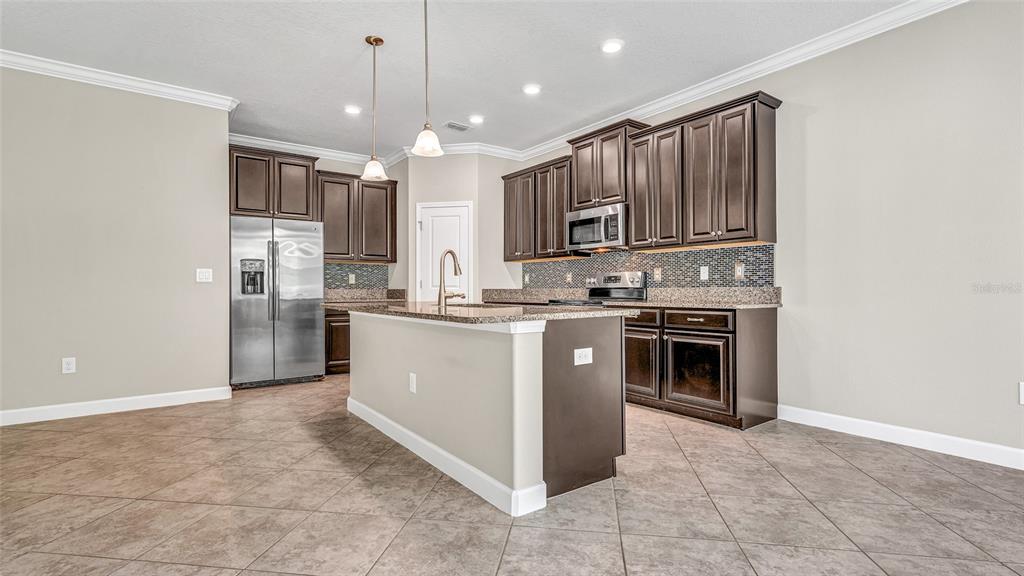 1695 Ludington Avenue Wesley Chapel, FL 33543 - Photo 12 of 65 a kitchen with kitchen island granite countertop a stove top oven a sink and a refrigerator