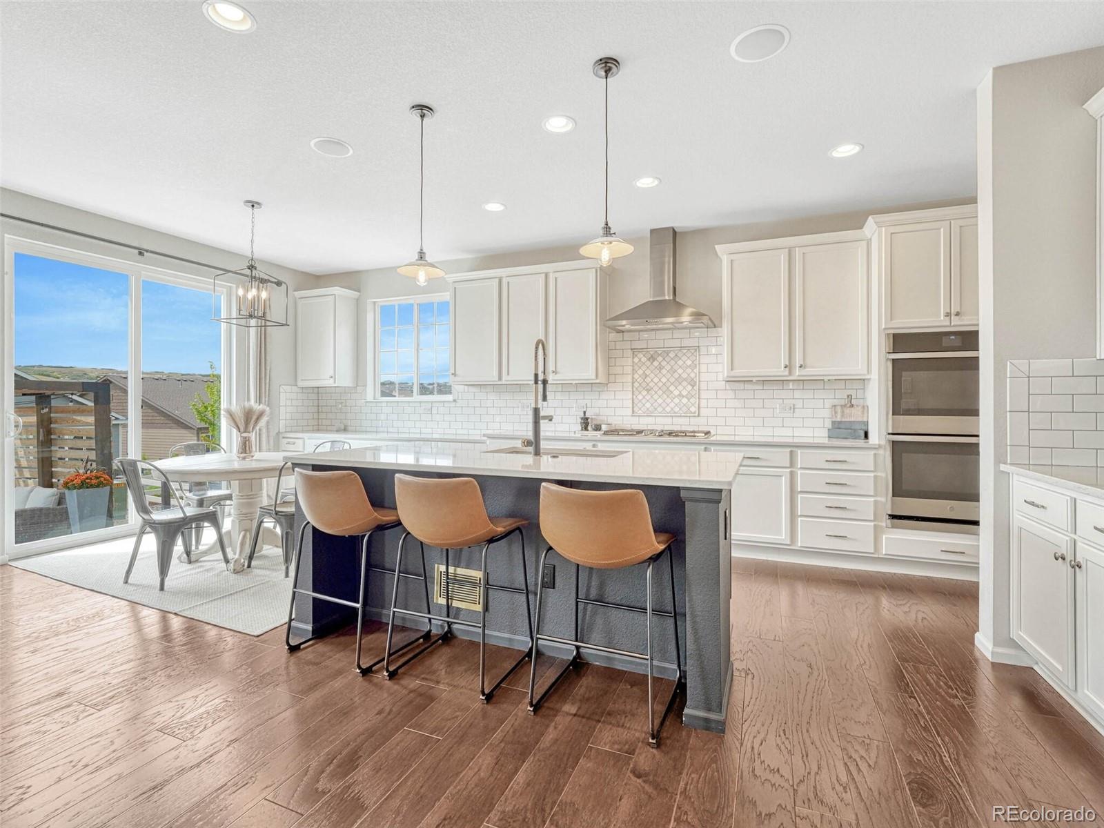 5921 Berry Ridge Wy. Castle Rock, CO 80104 - Photo 9 of 43 a kitchen with stainless steel appliances granite countertop a stove a sink a window and chairs with wooden floor
