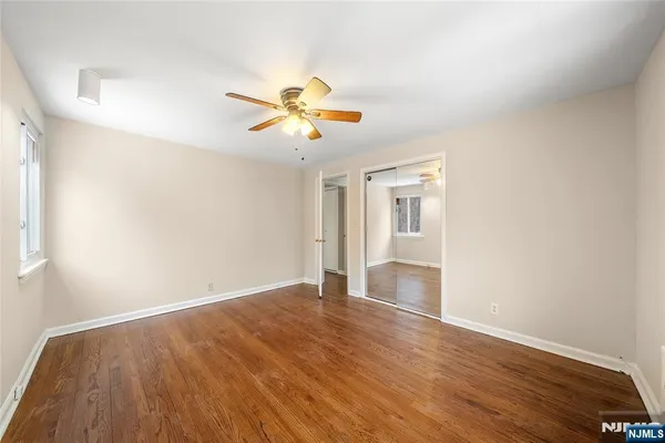 an empty room with wooden floor chandelier fan and windows