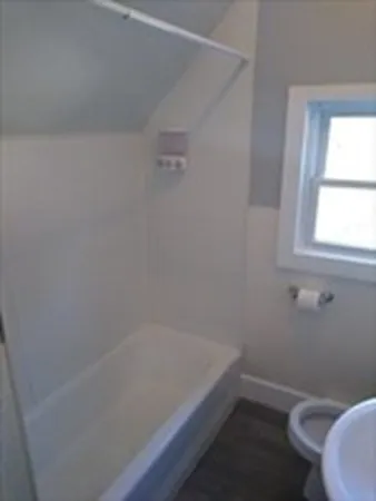 a bath tub sitting next to a white toilet and a window
