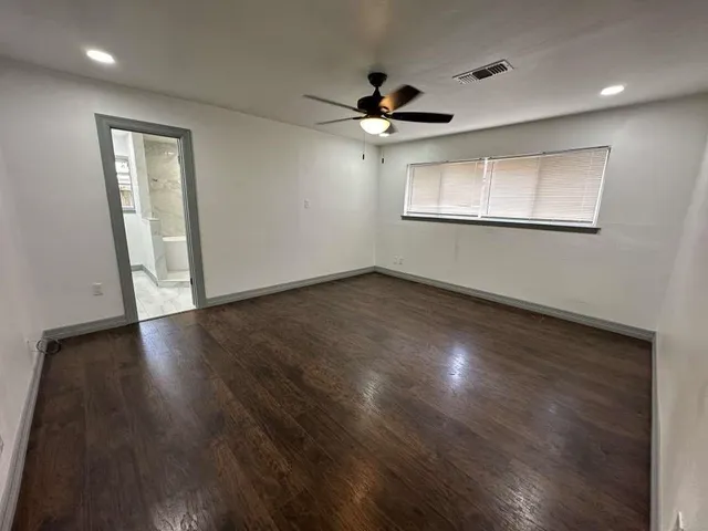 a view of an empty room with wooden floor and a ceiling fan