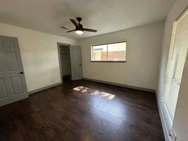 an empty room with wooden floor chandelier fan and windows