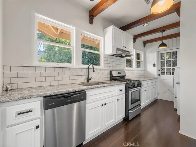 a kitchen with stainless steel appliances granite countertop white cabinets a sink a stove a refrigerator and island with wooden floor