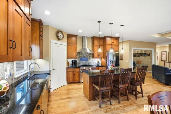a kitchen with stainless steel appliances granite countertop a stove top oven a sink a dining table and chairs with wooden floor
