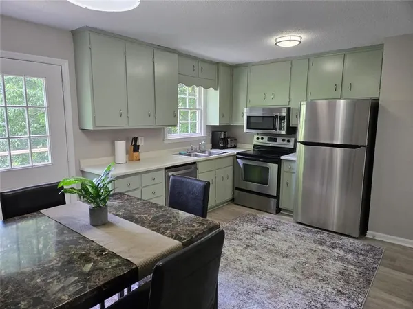 a kitchen with stainless steel appliances granite countertop a refrigerator a sink a stove a dining table and chairs