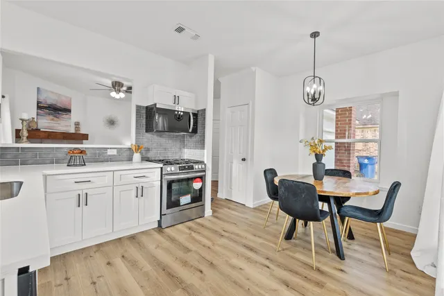 a kitchen with stainless steel appliances a dining table chairs a stove top oven a sink and dishwasher a refrigerator with wooden floor