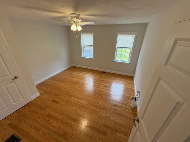 a view of empty room with wooden floor and fan