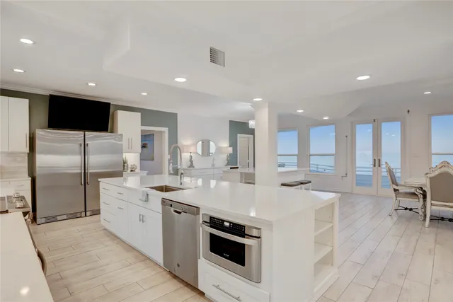 a large white kitchen with a large counter top space a sink stainless steel appliances and cabinets