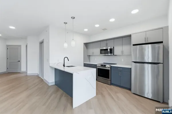 a kitchen with stainless steel appliances granite countertop a refrigerator a sink a stove and white cabinets with wooden floor