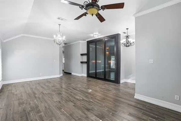 a view of an empty room with wooden floor and a ceiling fan