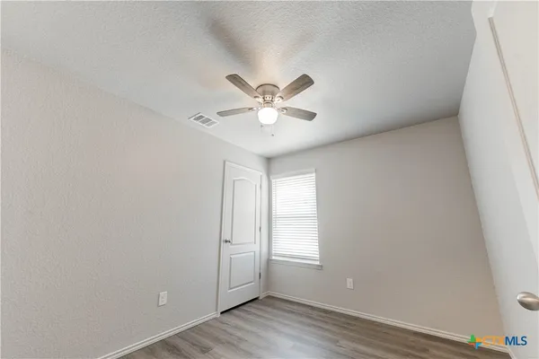 an empty room with wooden floor fan and windows