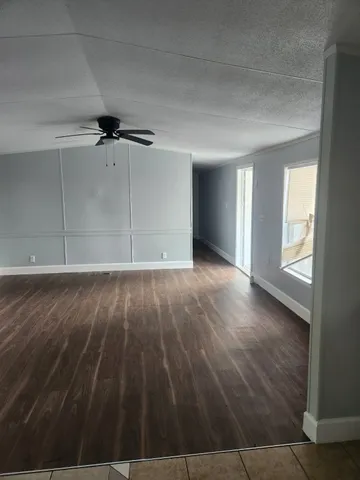 an empty room with wooden floor chandelier fan and windows