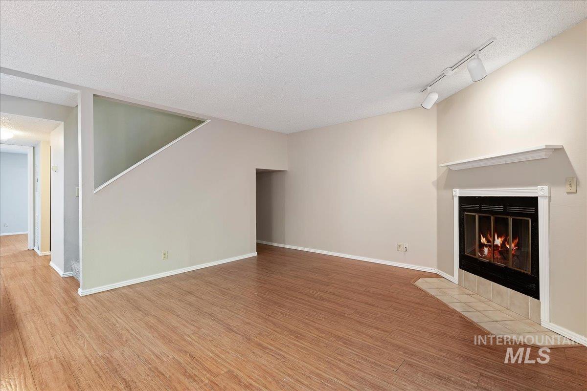 3611 South Gekeler Lane, Unit 124 Boise, ID 83706 - Photo 3 of 27 Unfurnished living room featuring track lighting, a textured ceiling, a fireplace with flush hearth, and wood finished floors