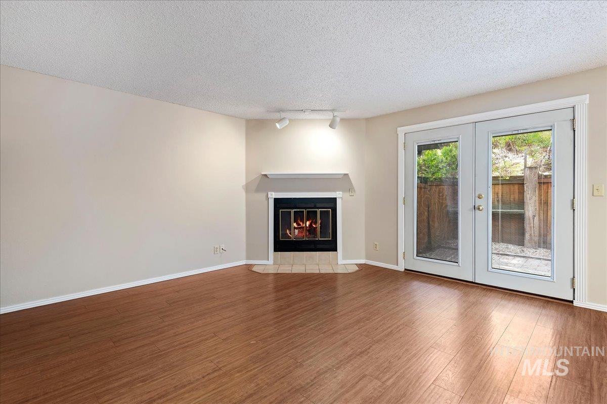 3611 South Gekeler Lane, Unit 124 Boise, ID 83706 - Photo 4 of 27 Unfurnished living room featuring a textured ceiling, french doors, wood finished floors, a fireplace with flush hearth, and rail lighting