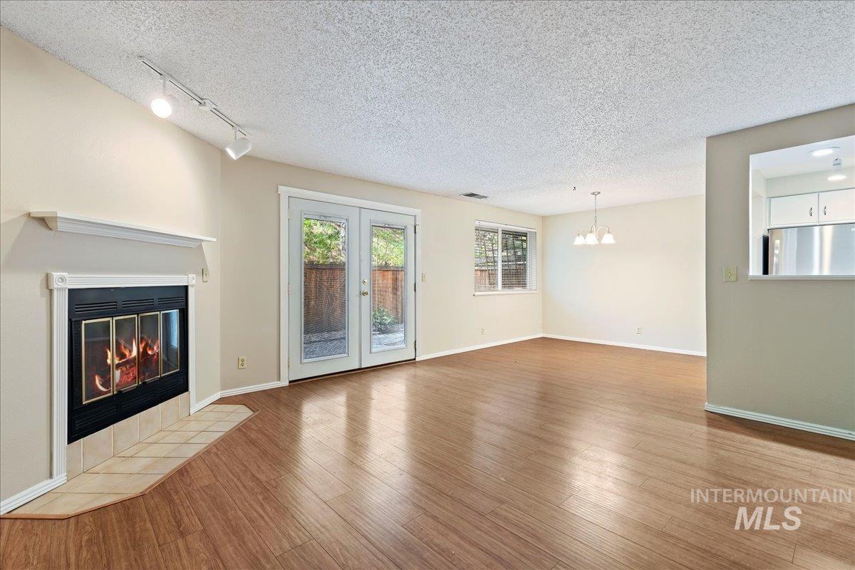 3611 South Gekeler Lane, Unit 124 Boise, ID 83706 - Photo 5 of 27 Unfurnished living room featuring wood finished floors, a textured ceiling, a tiled fireplace, french doors, and suspended lighting