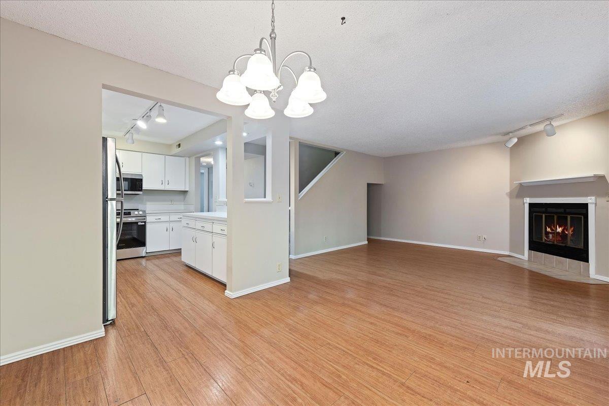 3611 South Gekeler Lane, Unit 124 Boise, ID 83706 - Photo 6 of 27 Unfurnished living room with a fireplace with flush hearth, a chandelier, a textured ceiling, and light wood-style floors