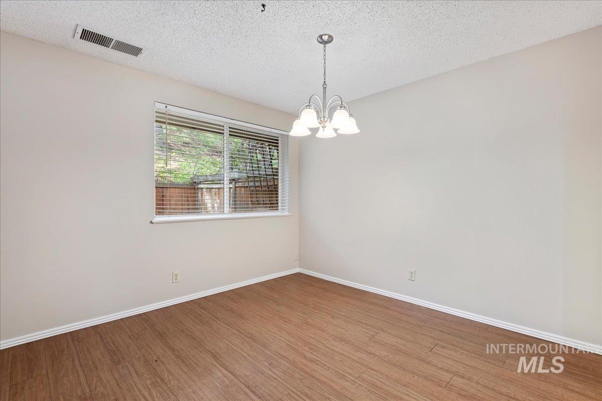 3611 South Gekeler Lane, Unit 124 Boise, ID 83706 - Photo 7 of 27 Empty room featuring suspended lighting, a textured ceiling, and wood finished floors