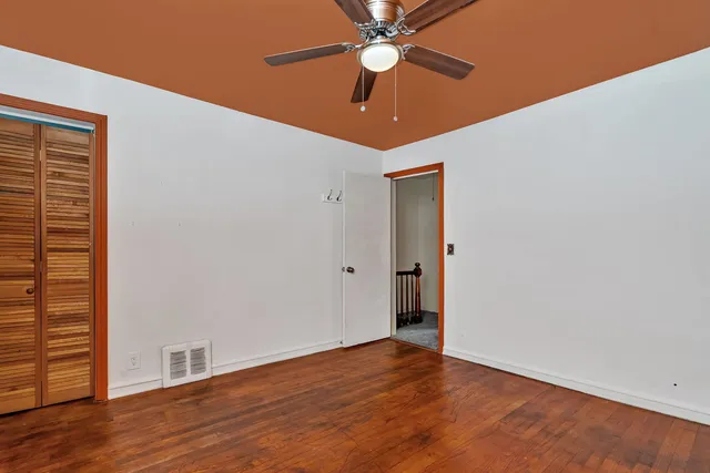 a view of an empty room with wooden floor and a ceiling fan