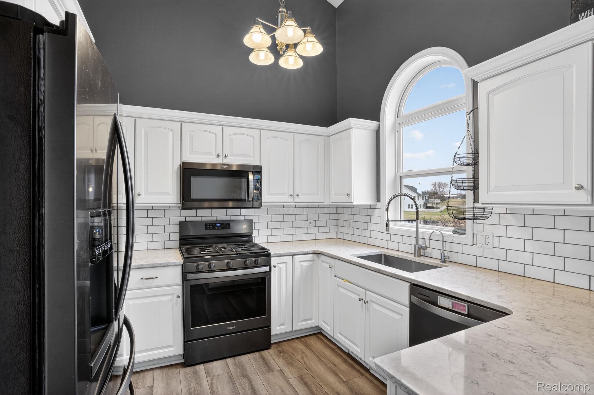 9055 Hegel Road Grand Blanc, MI 48439 - Photo 28 of 62 Kitchen featuring an arched window, white cabinetry, subway tile backsplash, light-toned countertops, and wood-finish flooring