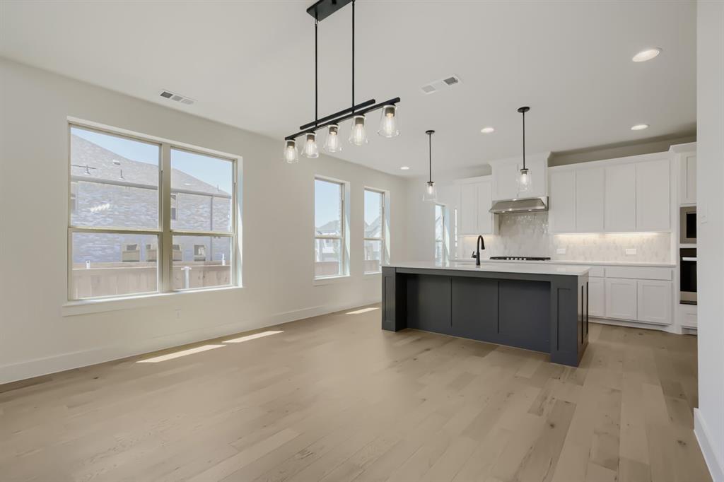 824 Stone Grv Road Lavon, TX 75166 - Photo 10 of 26 Open-concept living space featuring wood-finish flooring, a contemporary kitchen island with a light-colored countertop, recessed lighting, and ample natural light from multiple windows