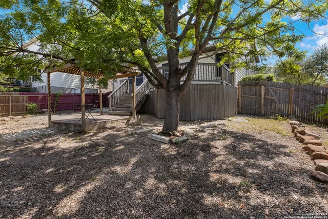 a view of a backyard with large trees and wooden fence