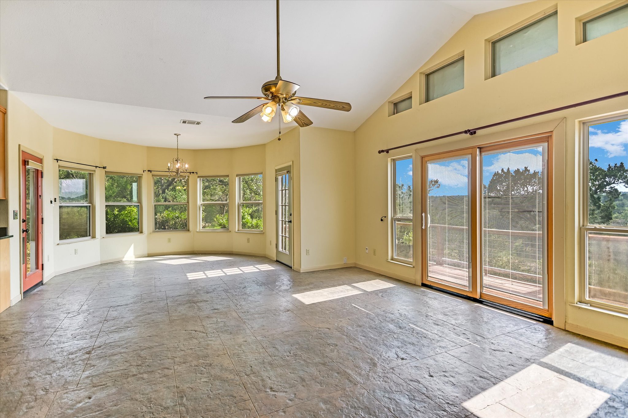 700 Cliffside Road Wimberley, TX 78676 - Photo 3 of 22 Vaulted ceiling with a ceiling fan, stamped concrete flooring, a curved wall with multiple windows, a sliding glass door leading to an outdoor space, and high transom windows